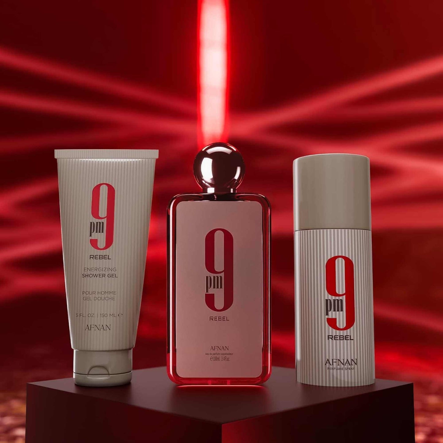 Bottles of shower gel, eau de parfum, and deodorant spray with Afnan 9PM Rebel branding on pedestal with a red laser firing background.