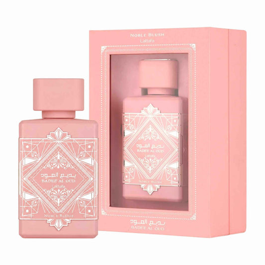 Pink Badee al Oud Noble Blush perfume bottle next to its pink presentation box, both featuring white geometric patterns and Arabic text.