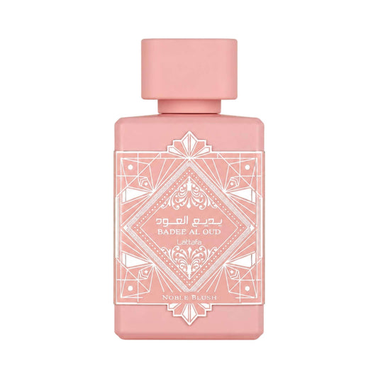 A rectangular pink perfume bottle with a matching pink cap, featuring white geometric and ornamental label detailing. The label reads 'Badee Al Qud' and 'Noble Blush'.